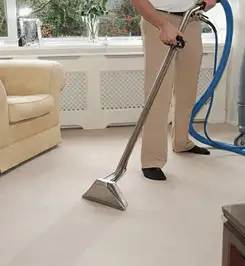 Professional carpet cleaner using a hot-water extraction wand and hose machine in a living room in Marietta, GA.