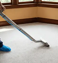 Steam carpet cleaning technician using a hot-water extraction wand on a residential carpet, wearing blue protective shoe covers Marietta, GA.