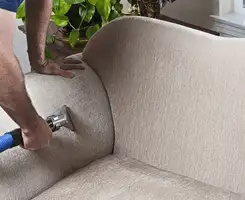 Professional upholstery cleaner deep-cleaning a fabric sofa with a handheld extraction tool and hose in Marietta, GA.